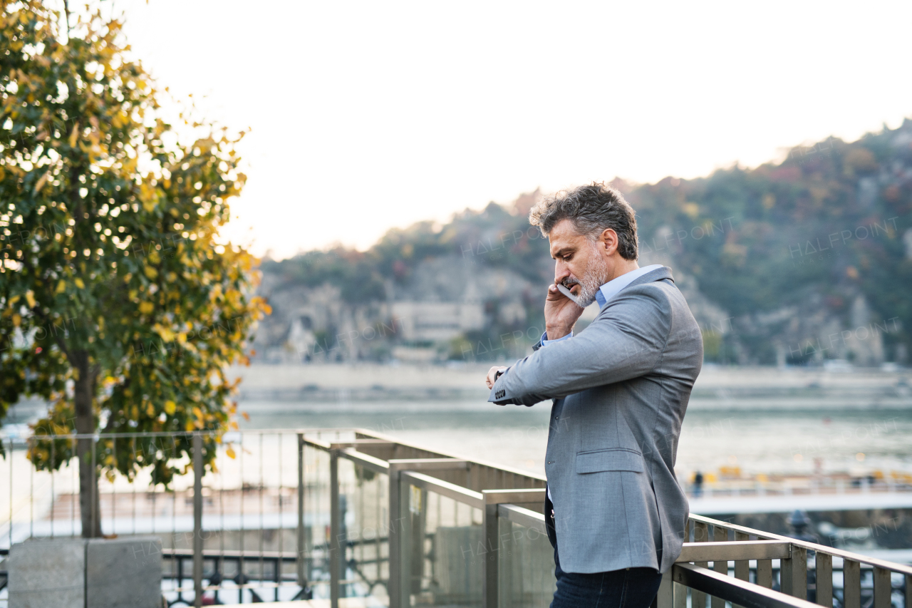 Handsome mature businessman with smartphone in a city. Man making a phone call, checking the time.