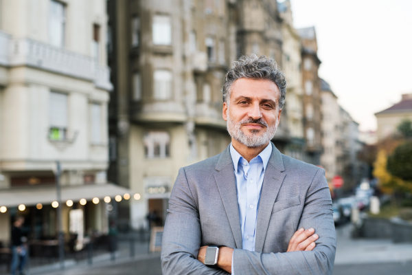 Handsome mature businessman with smartwatch in a city, arms crossed.