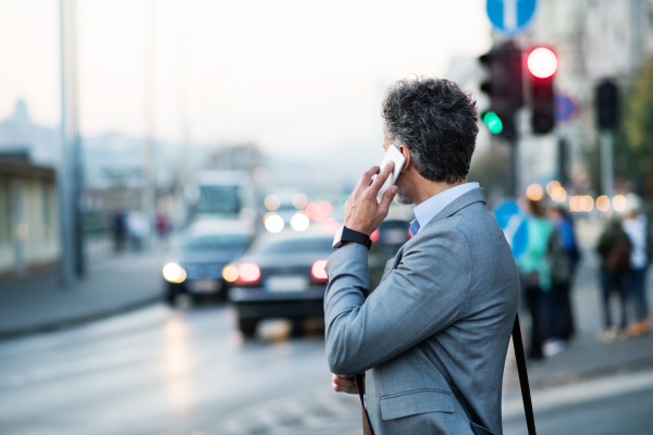 Handsome mature businessman with smartphone in a city, making a phone call.