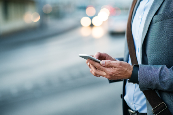 Unrecognizable businessman with smartphone in a city, text messaging.