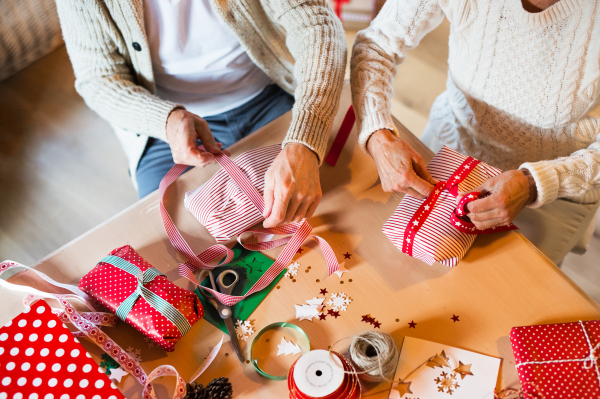 Unrecognizable senior couple in white woolen sweaters sitting at the table wrapping Christmas gifts together. Aerial view.