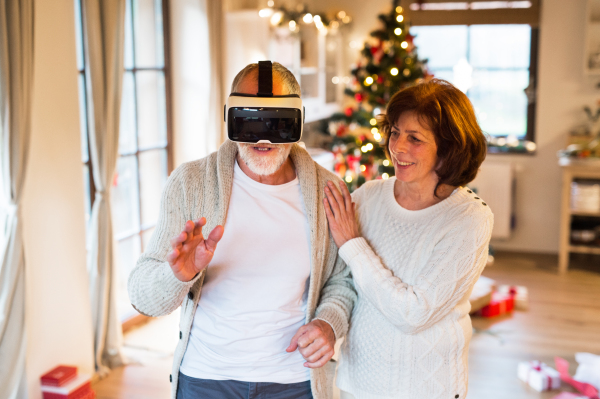 Senior couple in front of illuminated Christmas tree inside their house trying on VR glasses.