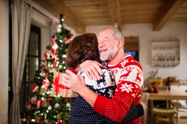 Senior couple a Christmas time. Woman is giving man a Christmas present. Close up.