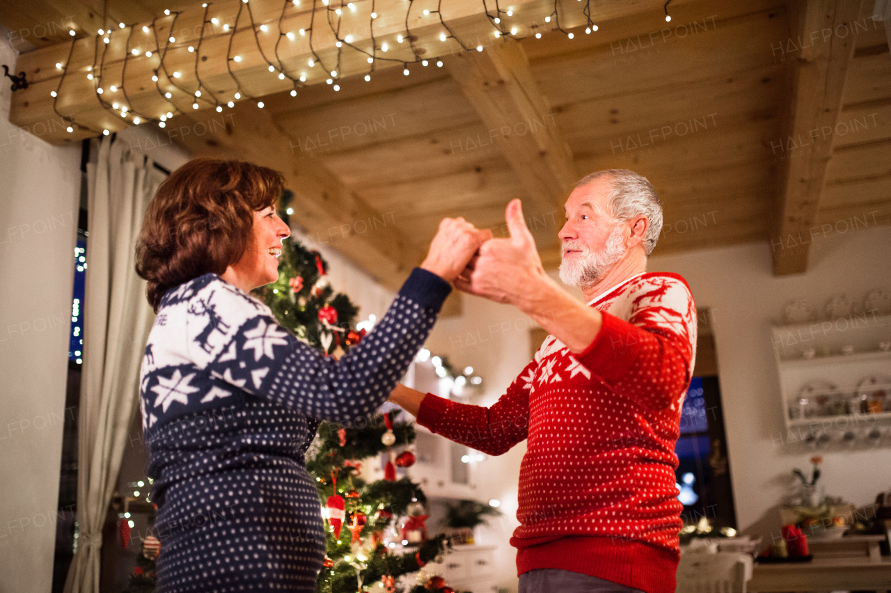 Beautiful senior couple in woolen sweaters with nordinc pattern dancing by Christmas tree in the evening.