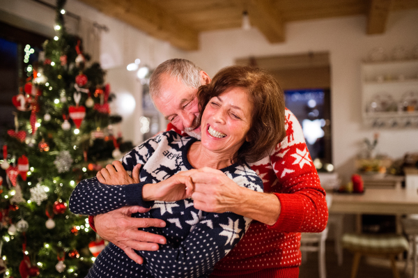 Beautiful senior couple in woolen sweaters with nordinc pattern at Christmas time, hugging. Man and woman having fun.