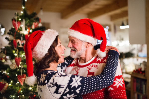 Beautiful senior couple in woolen sweaters with nordinc pattern at Christmas time, hugging. Man and woman wearing Santa hats.