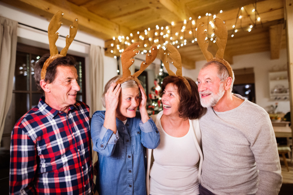 Senior friends wearing reindeer antlers headbands at Christmas time, having fun.