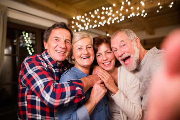 Senior friends at Christmas time, having fun. Two men and two women with smartphone taking selfie.