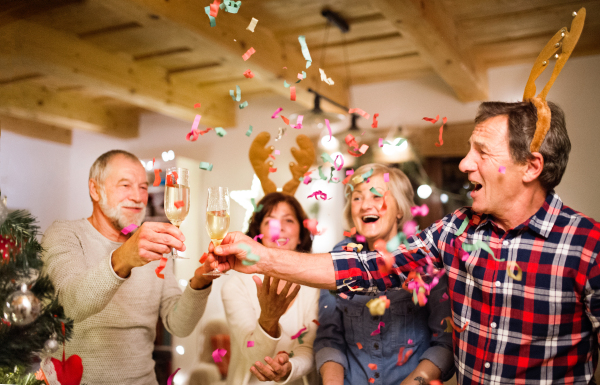 Senior friends with confetti and champagne next to Christmas tree, having fun.