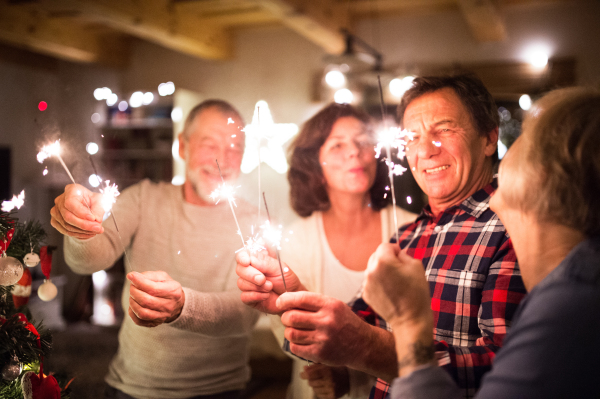 Senior friends with sparklers next to the illuminated Christmas tree, talking, having fun.