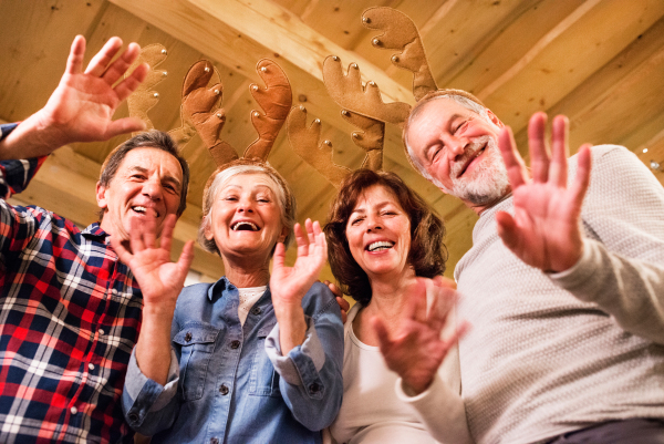 Senior friends with reindeer antlers headbands at Christmas time, waving and having fun.