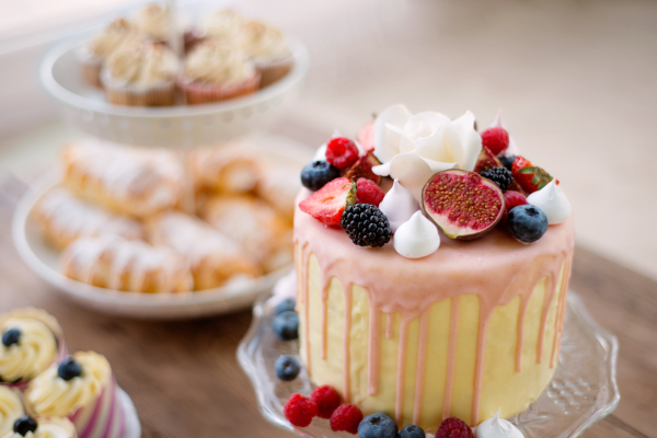 Cake with various berries and meringues on a stand. Cupcakes and tubes of pasty on other stand. Studio shot.