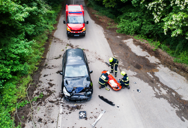 Three unrecognizable firefighters helping a young injured woman lying on the road after an accident. Top view.