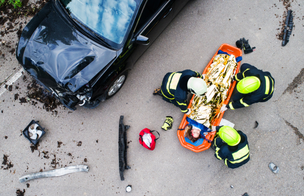 A young injured woman in a plastic stretcher after a car accident, covered by thermal blanket. Top view.