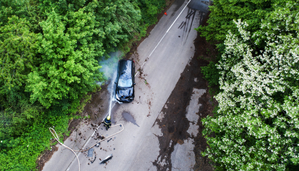 A firefighter extinguishing a burning car after an accident on the road in the countryside. Top view.