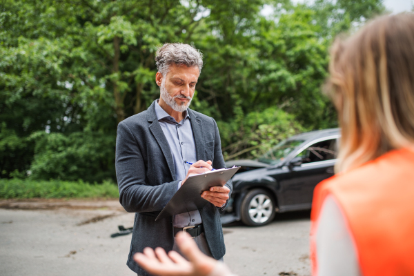 A man insurance agent talking to an unrecognizable woman outside on the road after a car accident.