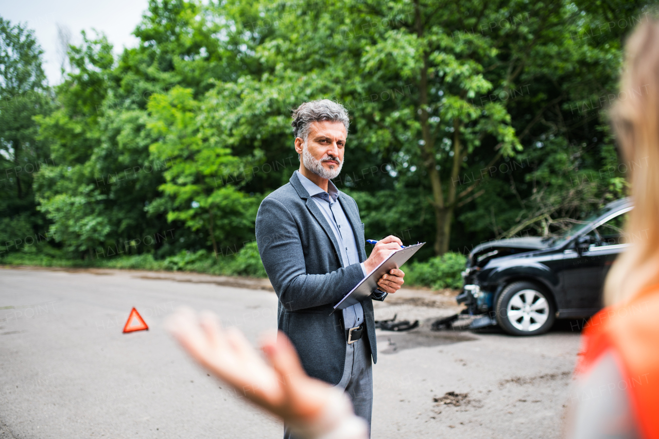 A man insurance agent talking to an unrecognizable woman outside on the road after a car accident.