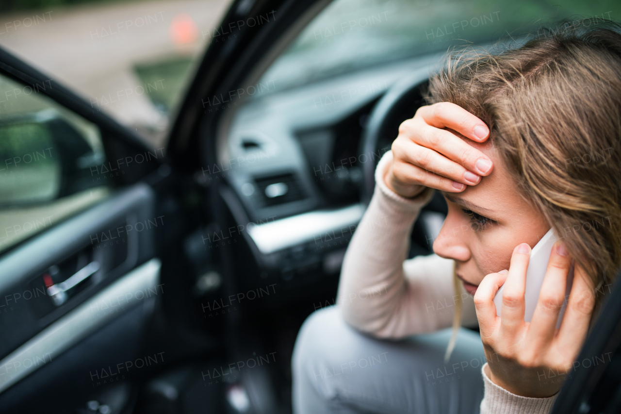 Young frustrated woman sitting in the damaged car after a car accident, making a phone call. A close-up.