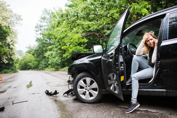 Young frustrated woman sitting in the damaged car after a car accident, making a phone call.