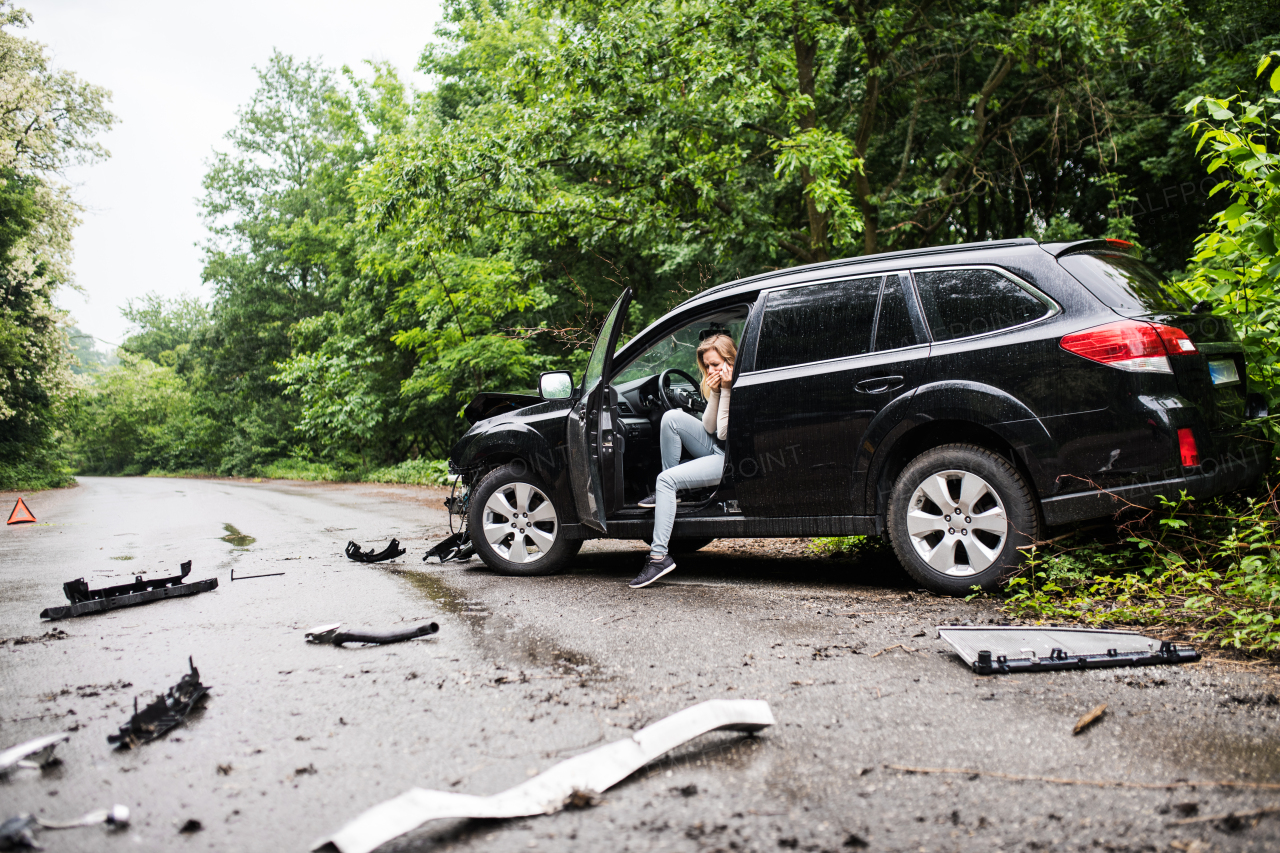 Young frustrated woman sitting in the damaged car after a car accident, making a phone call.