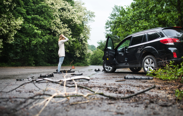 Young frustrated woman standing by the damaged car after a car accident.