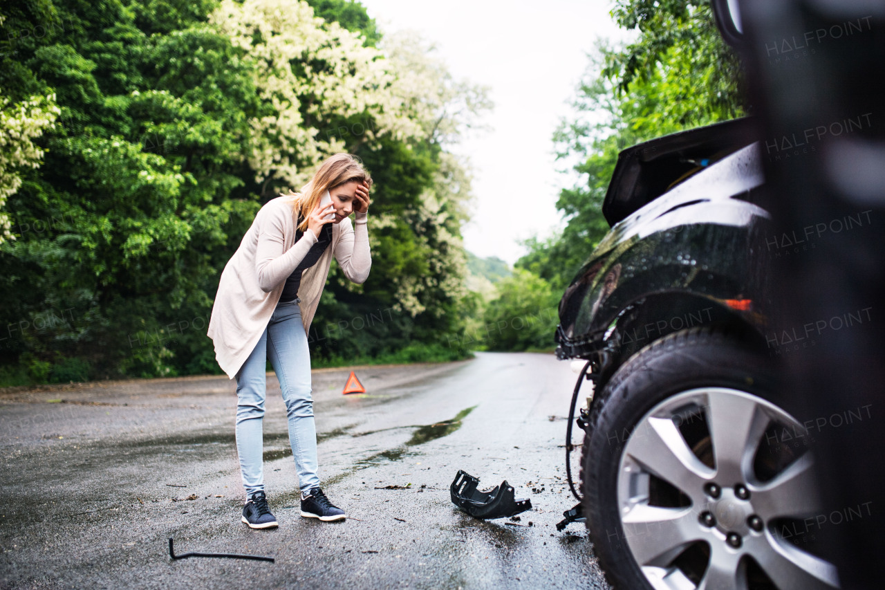 Young frustrated woman standing by the damaged car after a car accident, making a phone call.