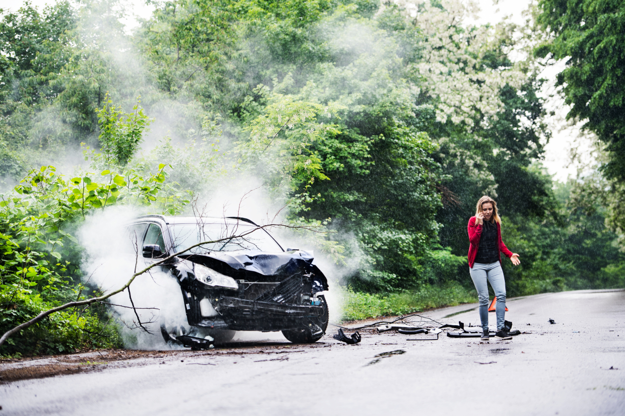 A frustrated young woman with smartphone by the damaged car after a car accident, making a phone call. Copy space.