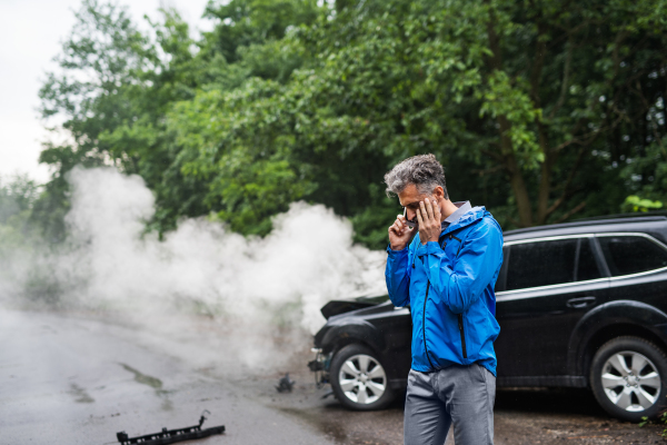 Handsome mature man making a phone call after a car accident, smoke in the background. Copy space.