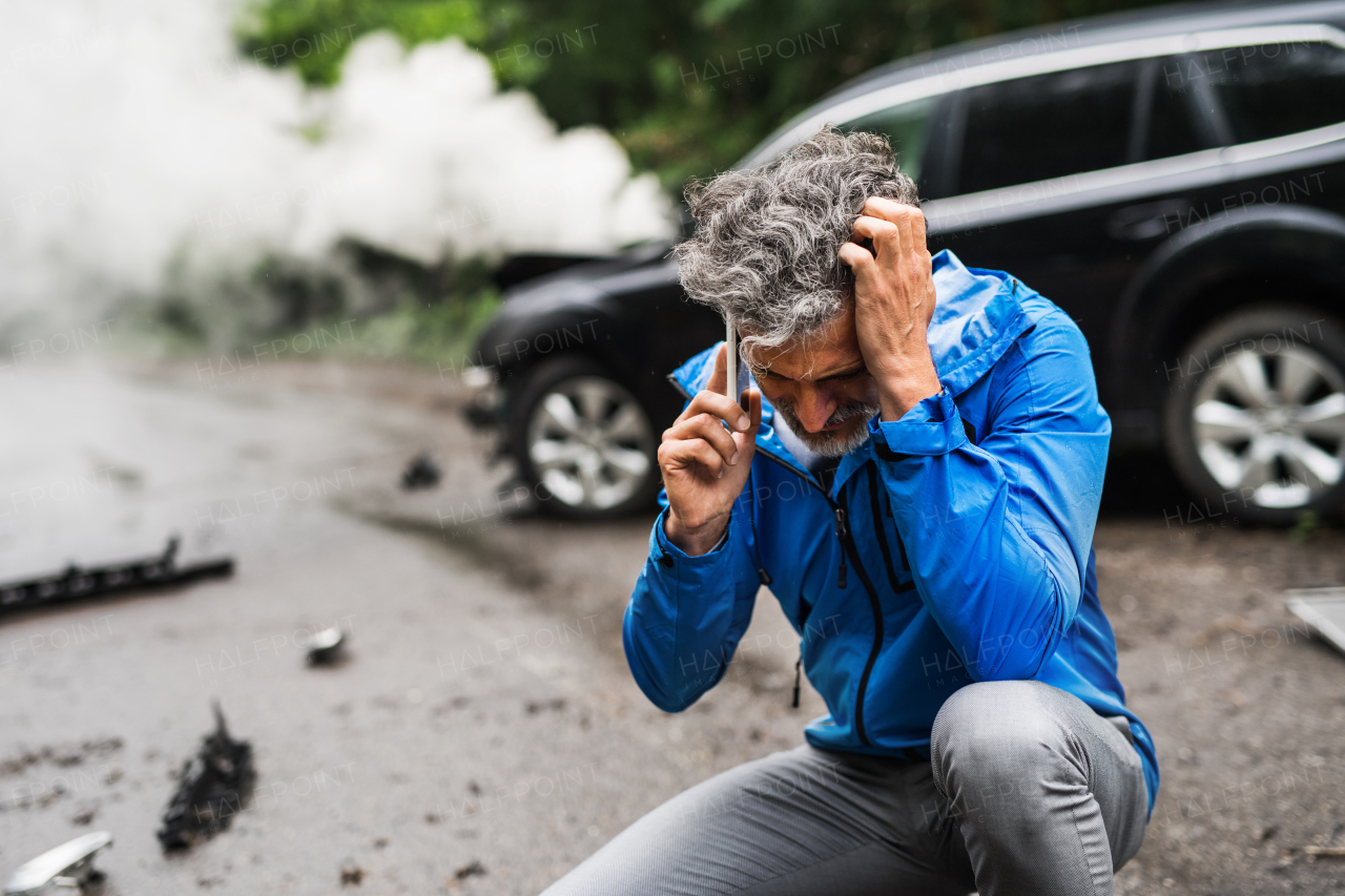 Handsome mature man making a phone call after a car accident, smoke in the background. Copy space.