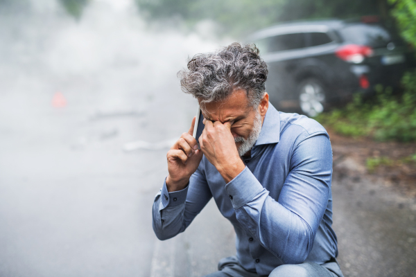 Handsome mature man making a phone call after a car accident, smoke in the background. Copy space.