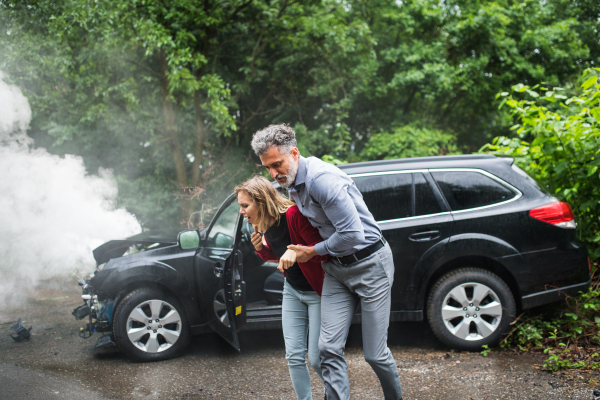 A mature man helping a young woman to walk away from the car after an accident.