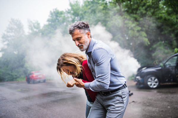 A mature man helping a young woman to walk away from the car after an accident.