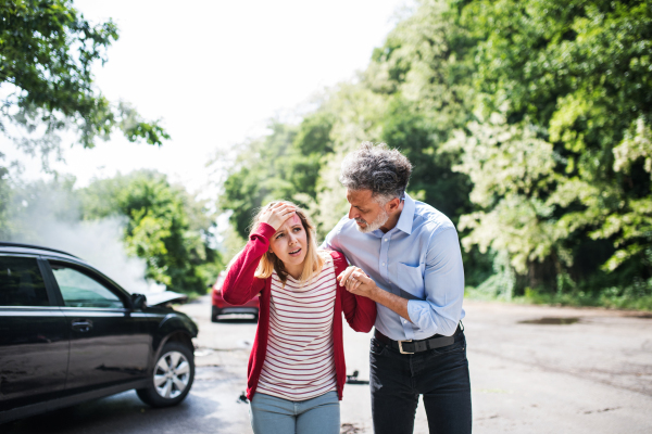 A mature man helping an injured young woman to walk away from the car after an accident.