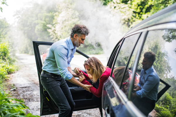 A mature man helping a young woman to get out of the car after a car accident.