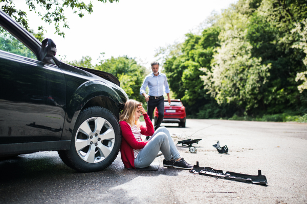 Young frustrated woman by the car after an accident and a mature man running towards her.