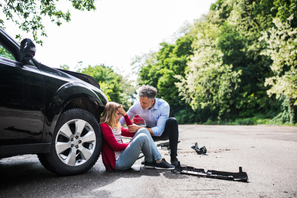 Young woman by the car after an accident and mature man helping her.