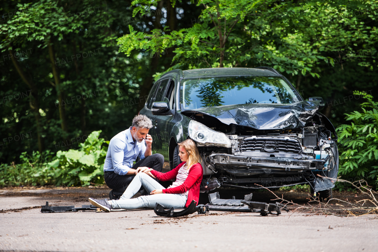 Young woman by the car after an accident and a man with smartphone, making a phone call.