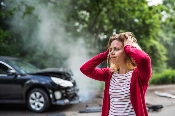 An injured young frustrated woman standing by the damaged car after a car accident.