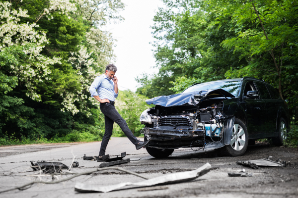 Mature handsome man standing by the car, making a phone call after a car accident.