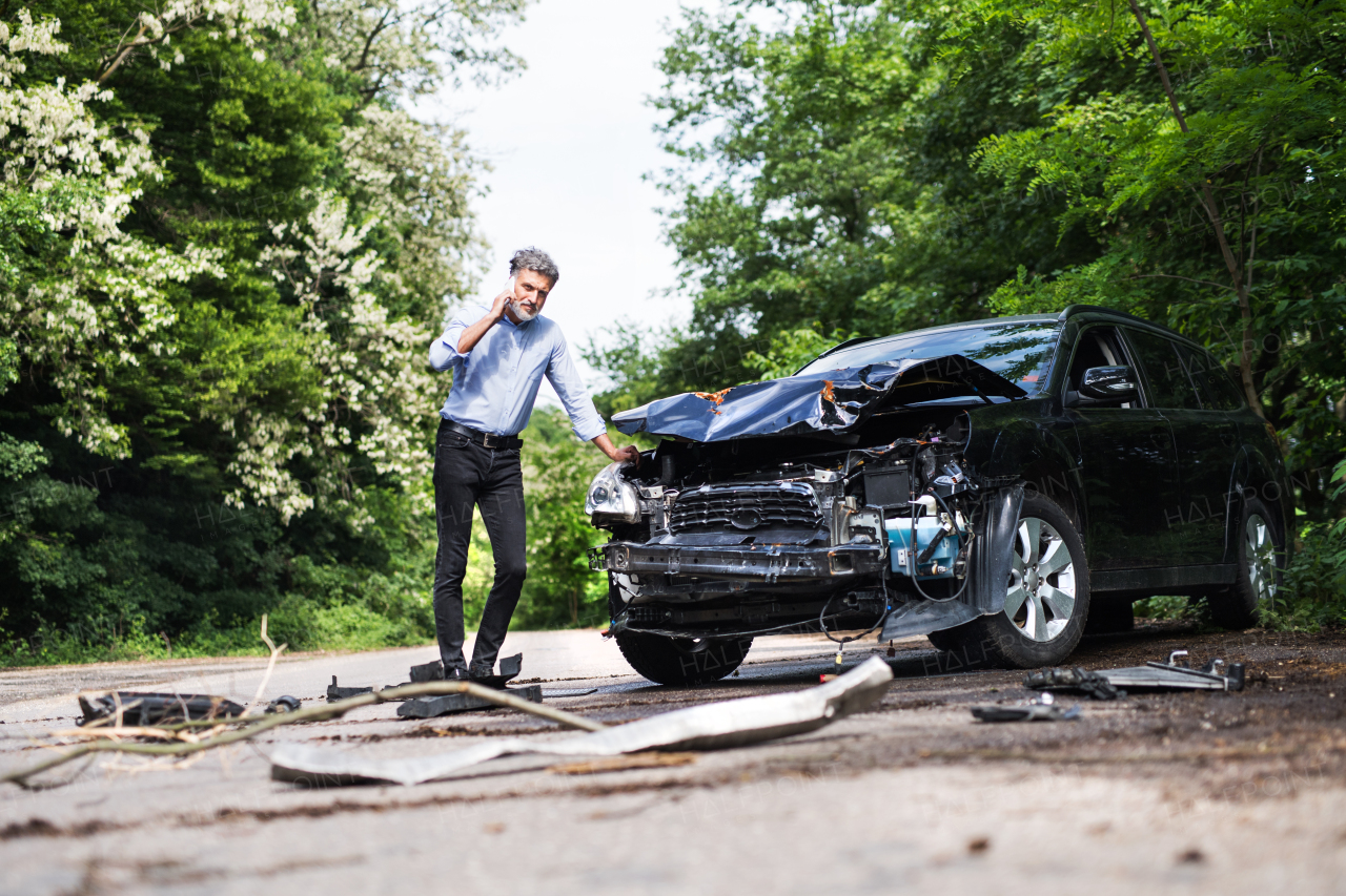 Mature handsome man standing by the car, making a phone call after a car accident.