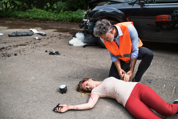 A man helping a young woman lying unconscious on the road after a car accident. Copy space.