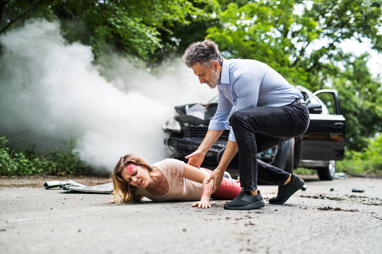 A man helping a young injured woman lying on the road after a car accident. Copy space.