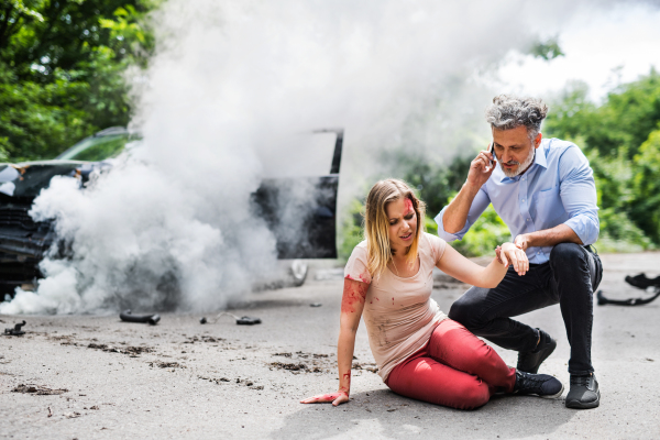 Young woman by the car after an accident and a man with smartphone, making a phone call.