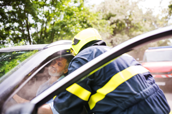 An unrecognizable firefighter getting an unconscious man out of the car after an accident.