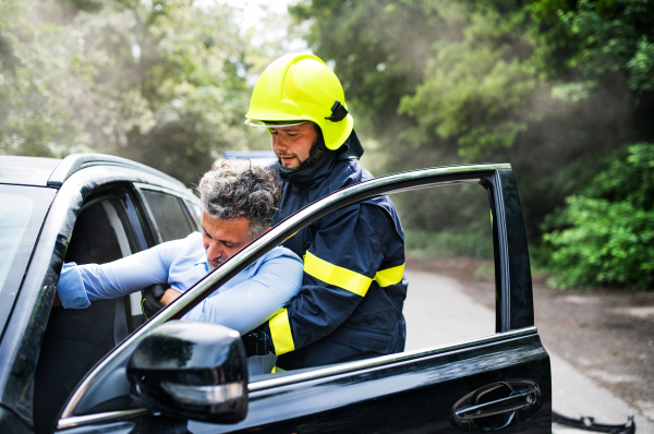 An unrecognizable firefighter getting an unconscious man out of the car after an accident.