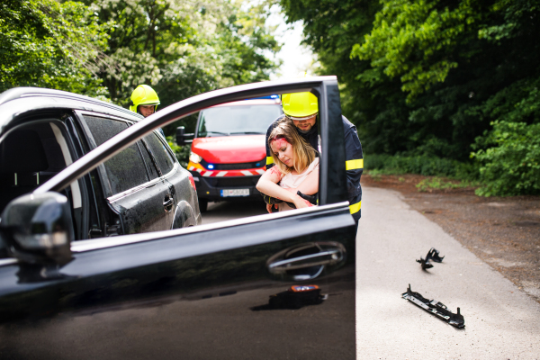 Two firefighters getting a young unconscious woman out of the car after an accident.