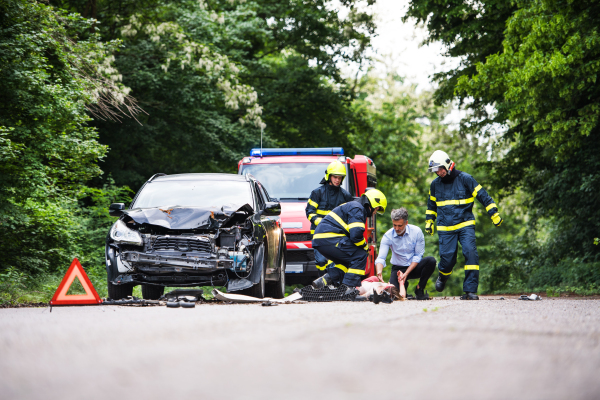 Three unrecognizable firefighters helping a young injured woman lying on the road after an accident.