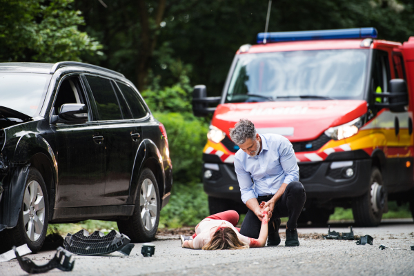 A man helping a young woman lying unconscious on the road after a car accident. Copy space.