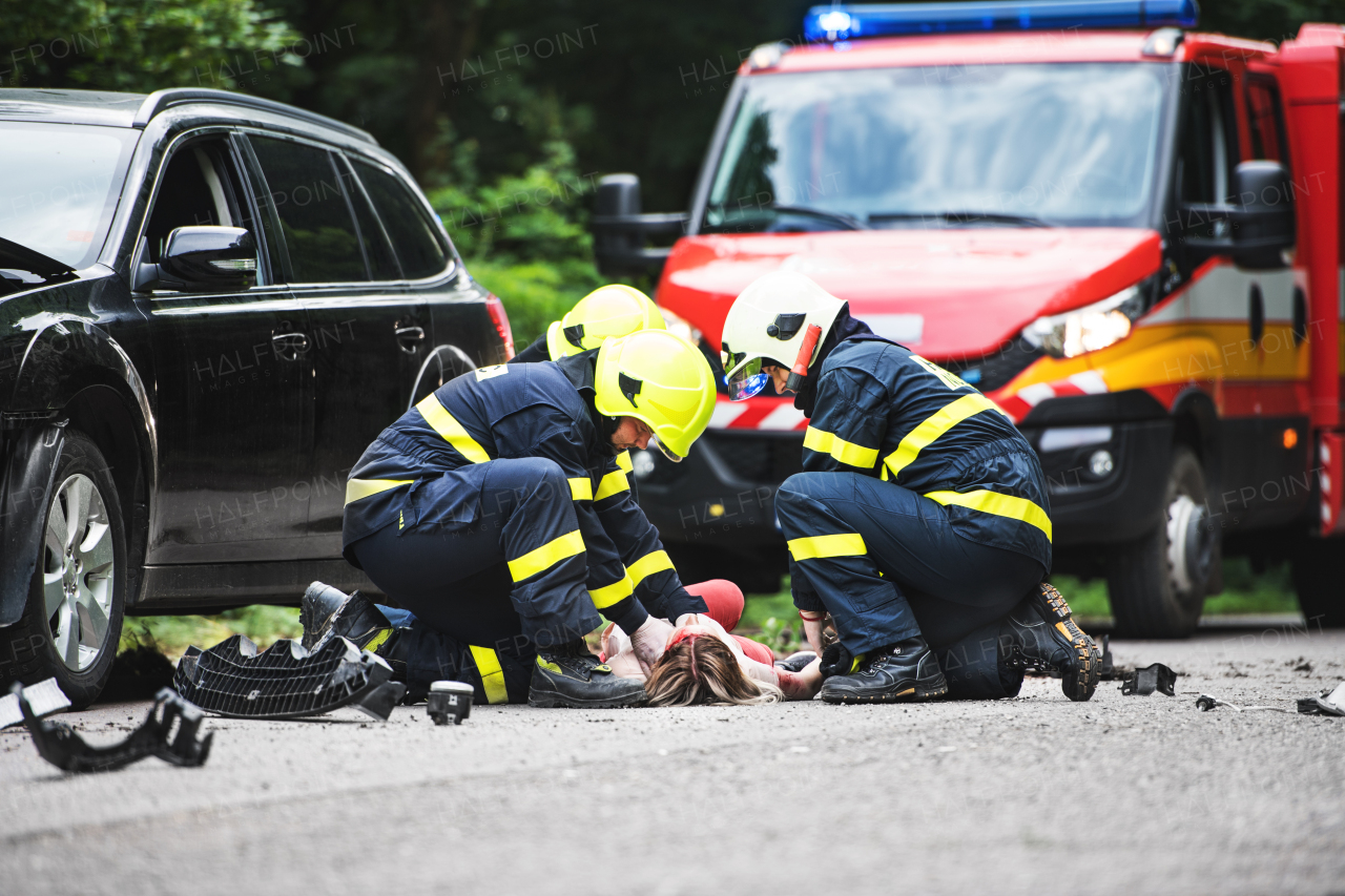 Firefighters helping a young woman after a car accident. A female driver lying down on the countryside road.