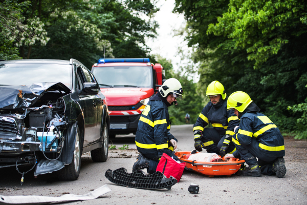 Firefighters helping a young woman after a car accident. A female driver in a plastic stretcher on the countryside road.